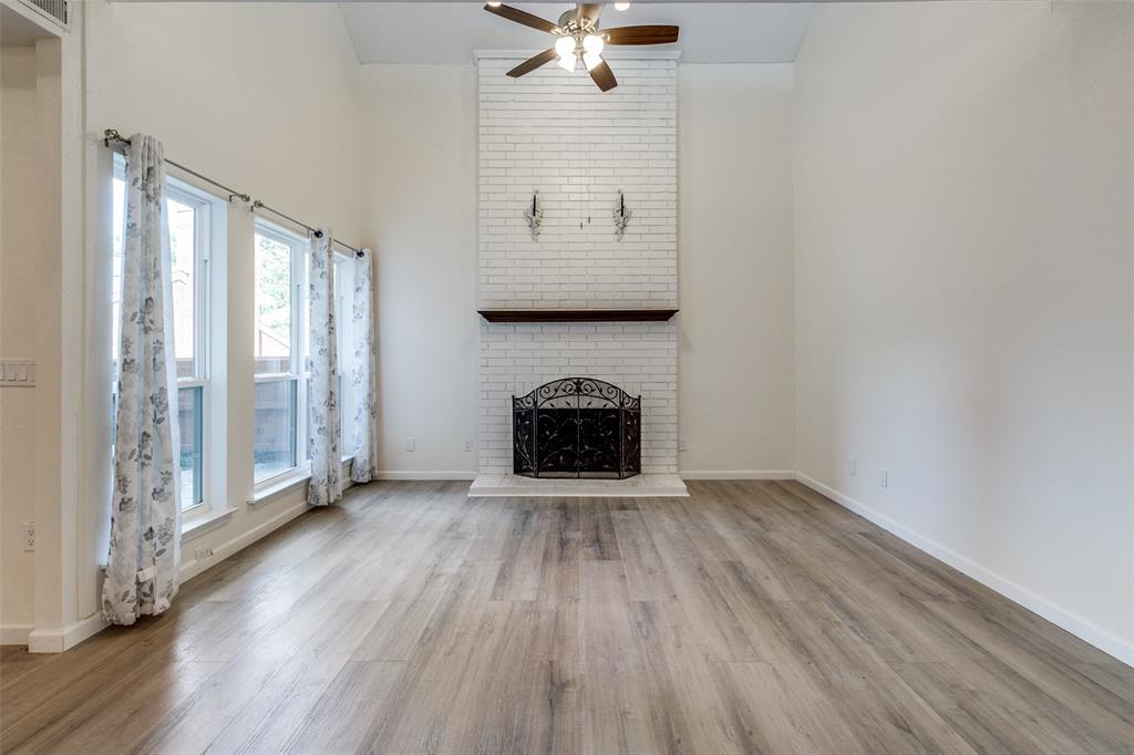 8404 Forest Lane, Unit 702 Dallas, TX 75243 - Photo 3 of 12 an empty room with windows a fireplace a ceiling fan and wooden floor