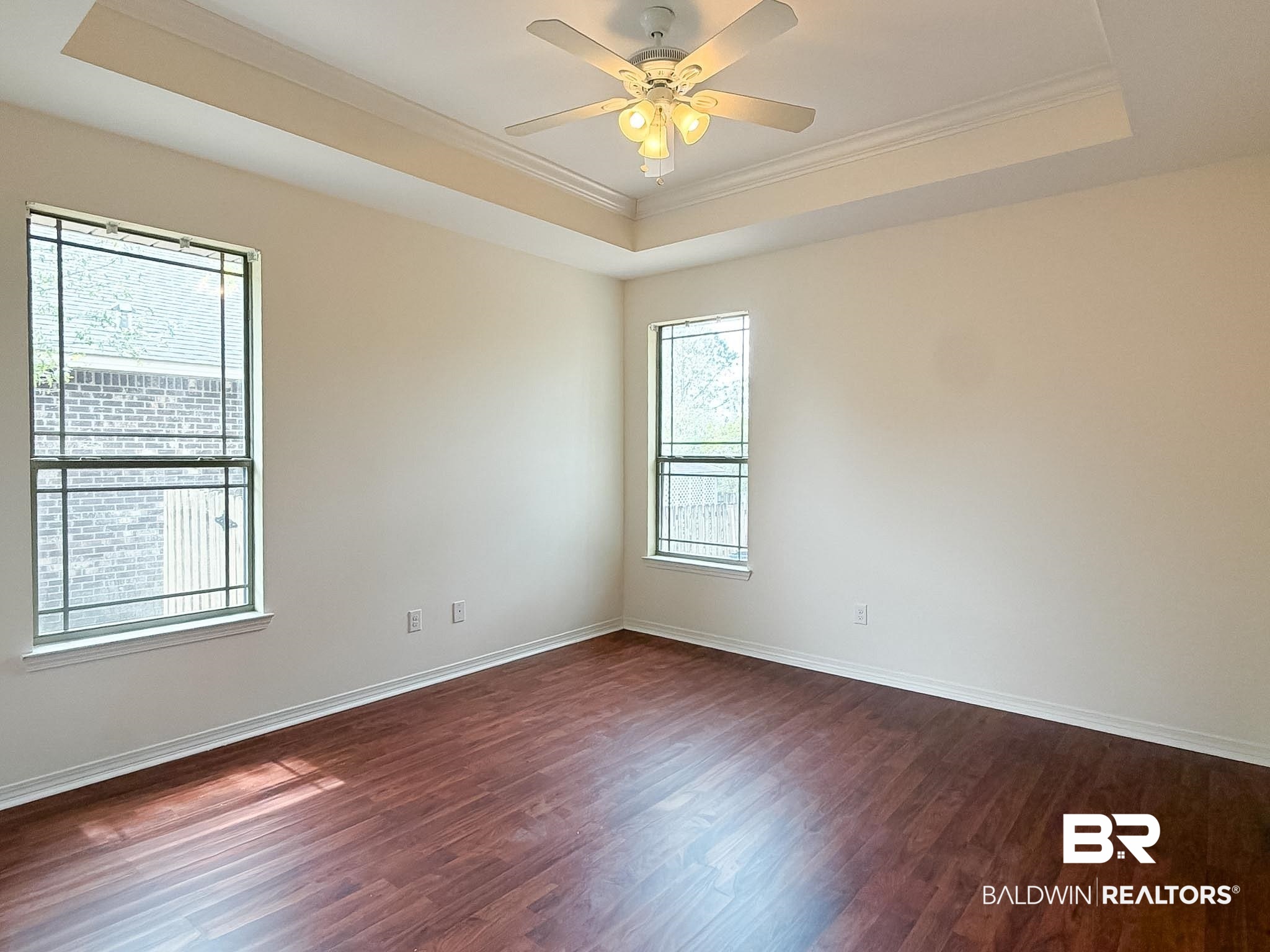 7332 Raintree Lane Gulf Shores, AL 36542 - Photo 9 of 21 Empty room featuring ornamental molding, dark wood-style floors, a ceiling fan, and a raised ceiling