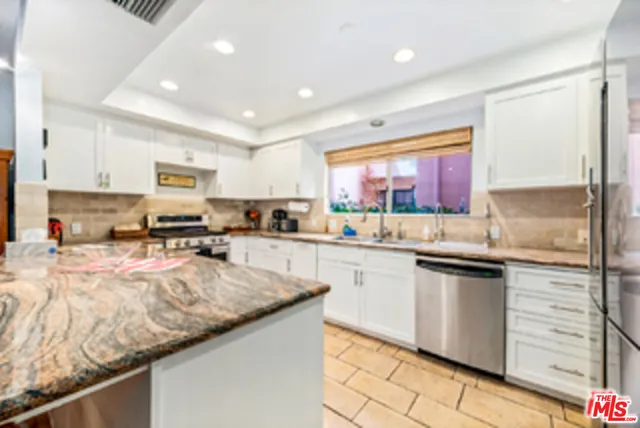 a kitchen with granite countertop kitchen island stainless steel appliances a sink stove top oven and refrigerator