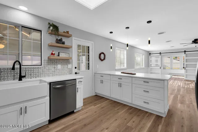 a large white kitchen with granite countertop a sink dishwasher a stove and white cabinets with wooden floor