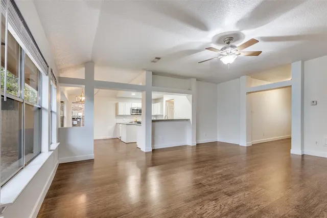 a view of an empty room with wooden floor and a kitchen