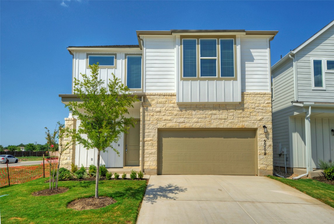 View of front of house with stone siding, board and batten siding, a garage, concrete driveway, and a front lawn