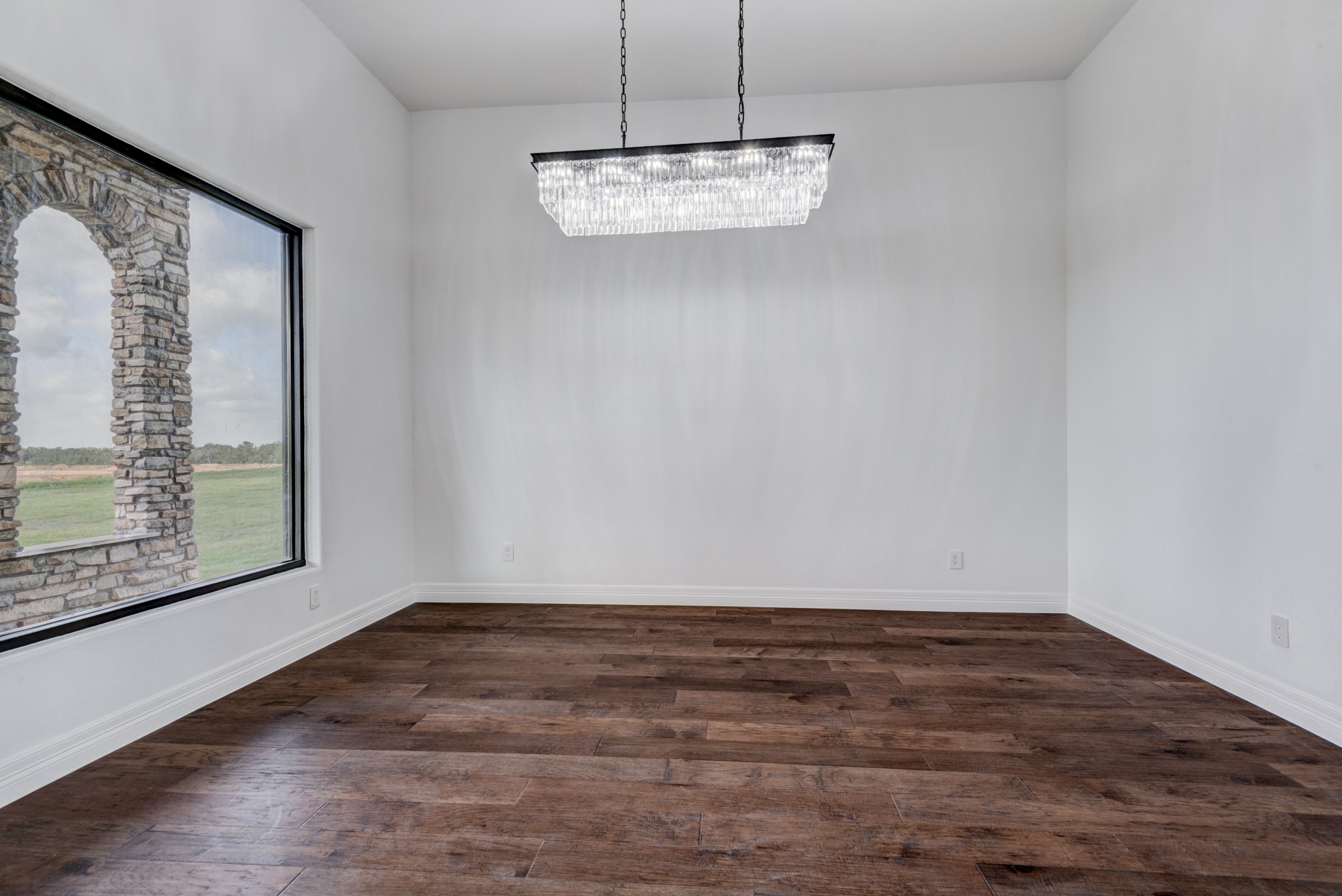 7348 Love Road Fulshear, TX 77441 - Photo 5 of 48 Elevate your dining experience in this elegant formal dining room, featuring rich hardwood floors, a striking modern chandelier, and a picturesque view through a large window with charming stone accents.