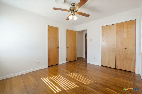 an empty room with wooden floor and a ceiling fan
