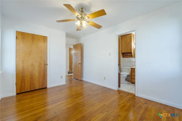 a view of an empty room with wooden floor and a ceiling fan