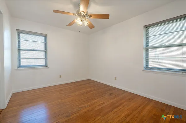 a view of empty room with wooden floor and fan