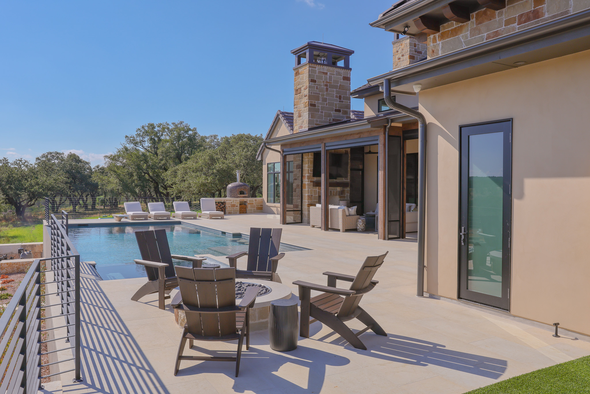 920 Ryan Road Bertram, TX 78605 - Photo 31 of 40 Stone chimneys and custom glass doors define the backyard terrace alongside a swimming pool.