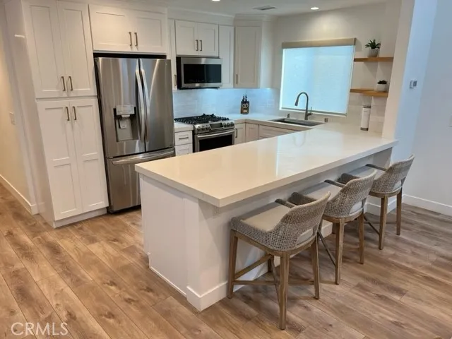 a kitchen with stainless steel appliances a refrigerator a stove a sink and white cabinets with wooden floor