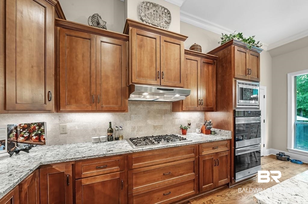 30014 Dolive Ridge Daphne, AL 36527 - Photo 20 of 57 Kitchen with appliances with stainless steel finishes, crown molding, light stone countertops, and tasteful backsplash