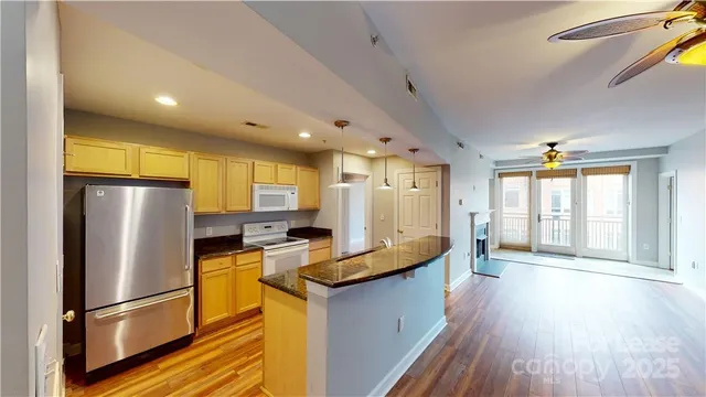 a kitchen with granite countertop a refrigerator a sink dishwasher a stove and white cabinets with wooden floor