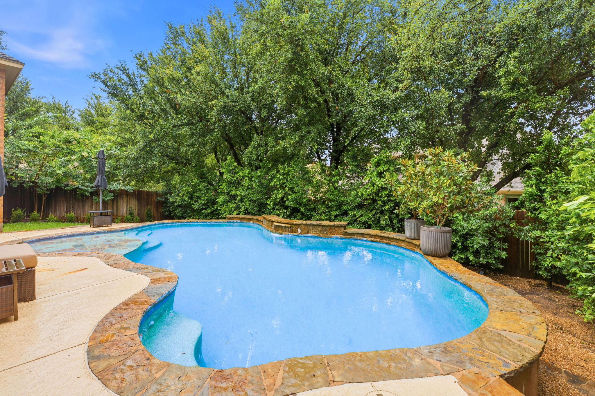 12321 Edenvale Path Austin, TX 78732 - Photo 35 of 36 A tranquil backyard oasis features a freeform pool surrounded by lush greenery and stone coping.