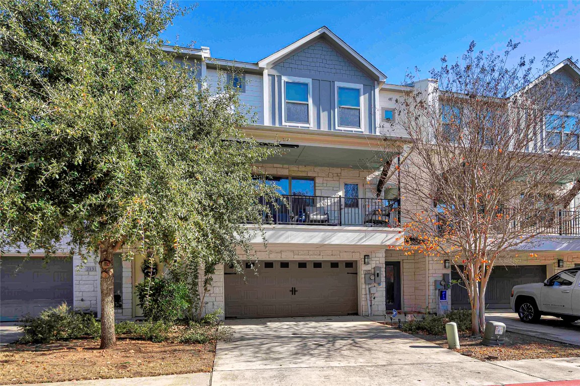 View of front of house featuring a balcony, stone siding, concrete driveway, and a garage