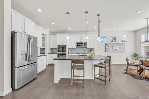 a kitchen with stainless steel appliances granite countertop a refrigerator a sink dishwasher a stove and white cabinets with wooden floor