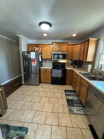 a kitchen with stainless steel appliances a stove a sink a refrigerator white cabinets a dining table and chairs