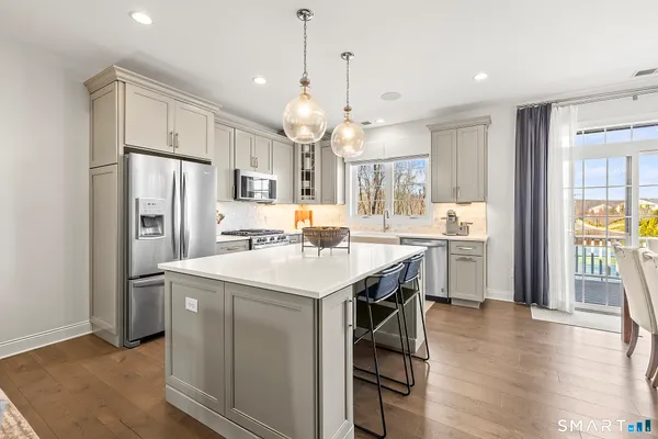a kitchen with stainless steel appliances a stove a sink a refrigerator and white cabinets with wooden floor