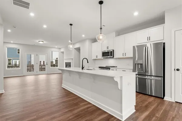a large kitchen with stainless steel appliances a refrigerator a stove a sink dishwasher a oven and a dining table with wooden floor
