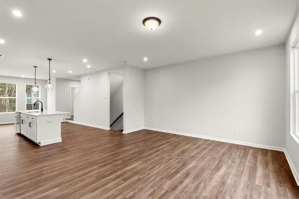 a view of an empty room and kitchen with wooden floor