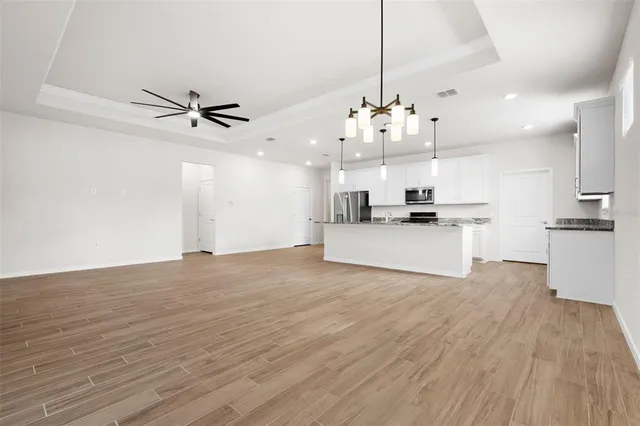 a kitchen with stainless steel appliances granite countertop a sink a stove a refrigerator and white cabinets with wooden floor