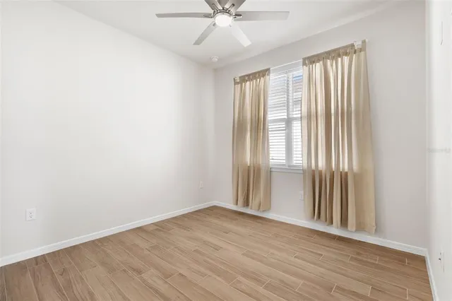 an empty room with wooden floor fan and windows