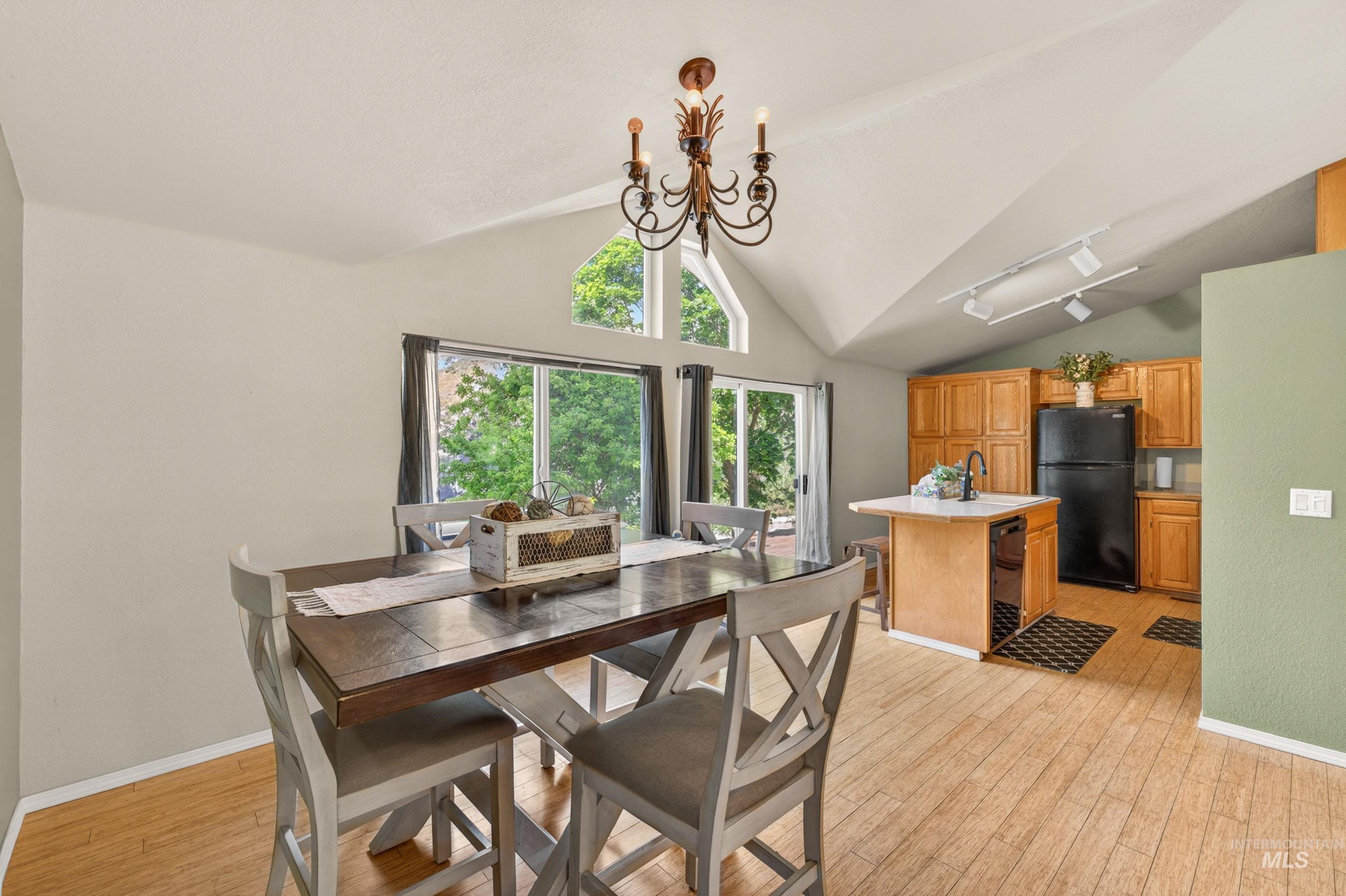 151 Cow Creek Road Lucile, ID 83542 - Photo 13 of 50 Vaulted ceiling with an ornate chandelier, large windows, and an open-concept kitchen with wood cabinetry, black appliances, and a central island