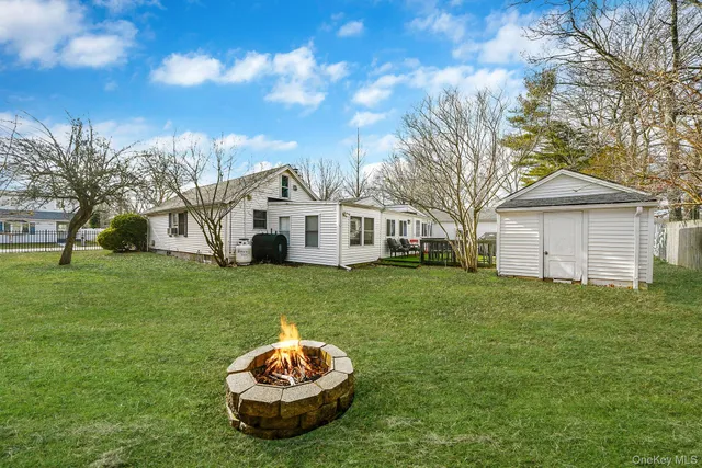 a view of a white house in a big yard with large trees and wooden fence
