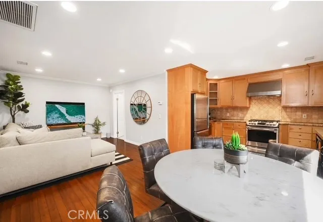 a living room with stainless steel appliances kitchen island granite countertop a couch a dining table and chairs with wooden floor