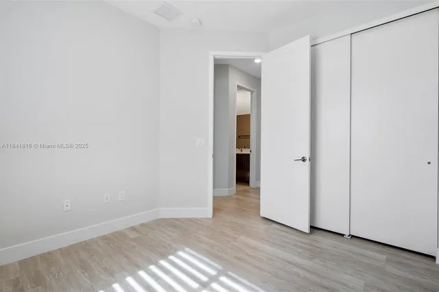 a view of an empty room with wooden floor and closet