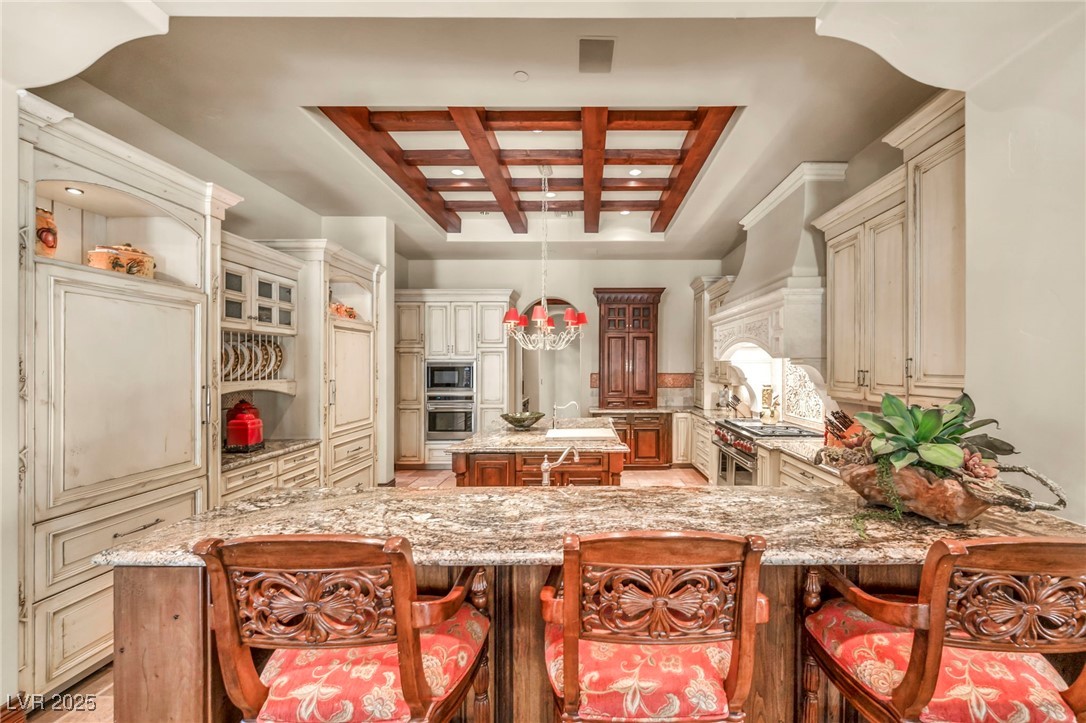 1793 Anelli Court Henderson, NV 89012 - Photo 29 of 47 Kitchen with coffered ceiling, light stone counters, cream cabinets, a center island, and a breakfast bar area