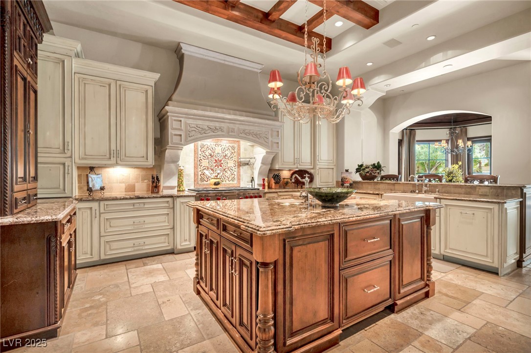 1793 Anelli Court Henderson, NV 89012 - Photo 3 of 47 Kitchen featuring cream cabinets, coffered ceiling, light stone countertops, beamed ceiling, and a chandelier