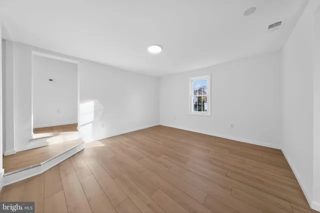 a view of empty room with wooden floor and kitchen view