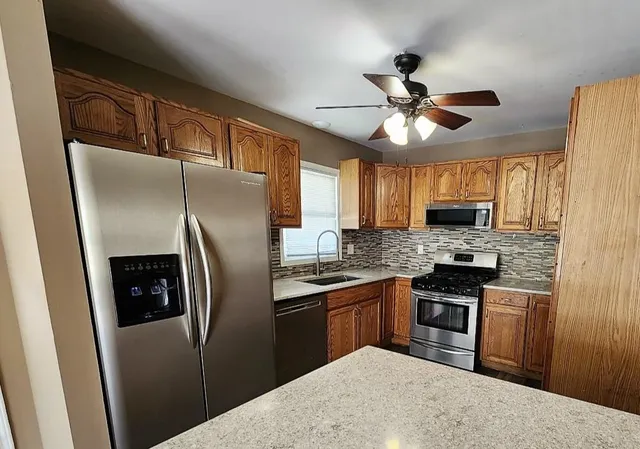 a kitchen with stainless steel appliances granite countertop a refrigerator a sink a stove top oven a kitchen island with cabinets and wooden floor