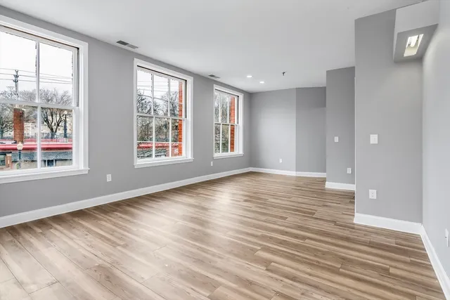 a view of an empty room with wooden floor and a window