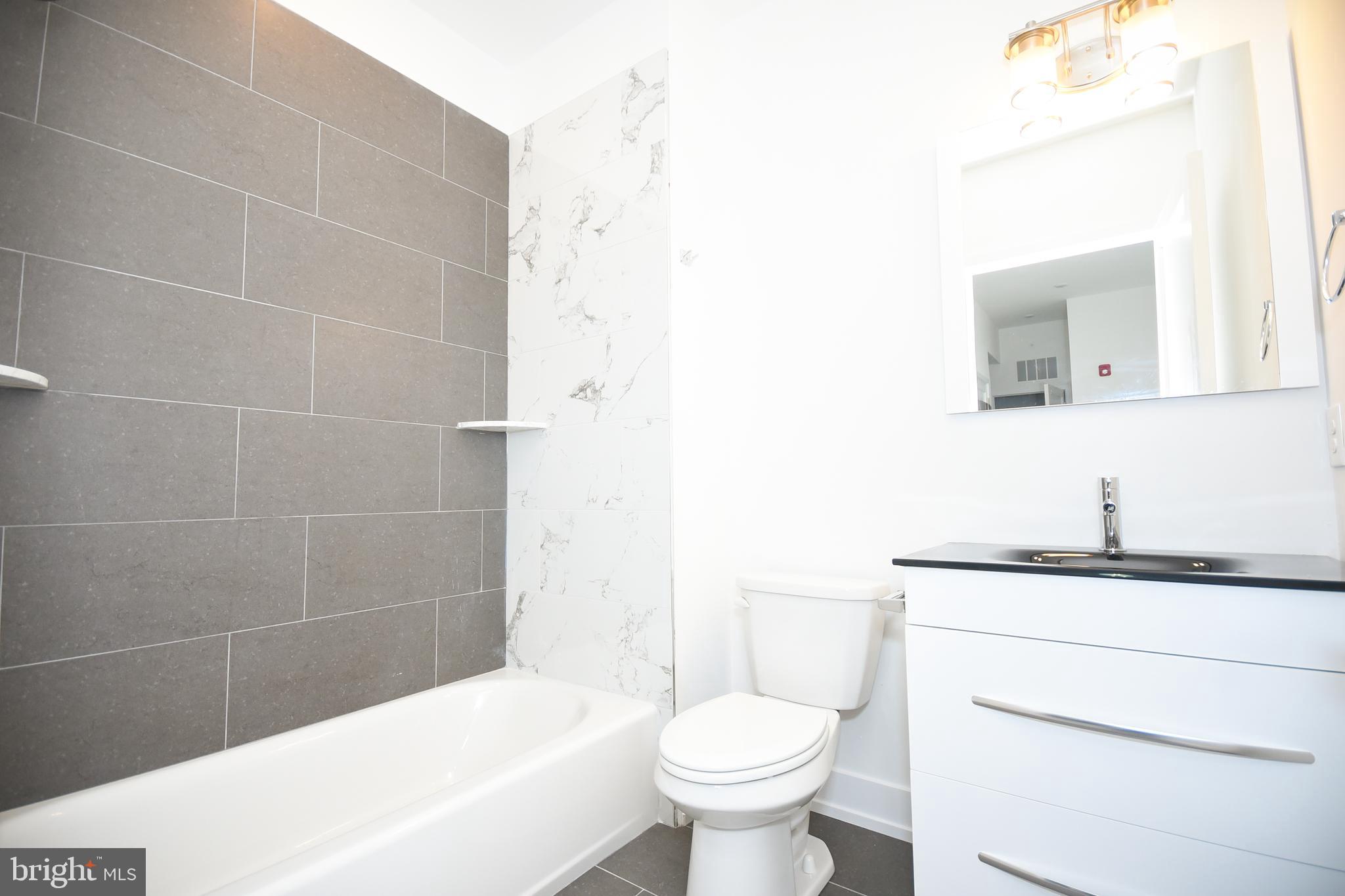 6162 Ridge Avenue, Unit 201 Philadelphia, PA 19128 - Photo 12 of 14 a bathroom with a granite countertop sink toilet mirror and bathtub