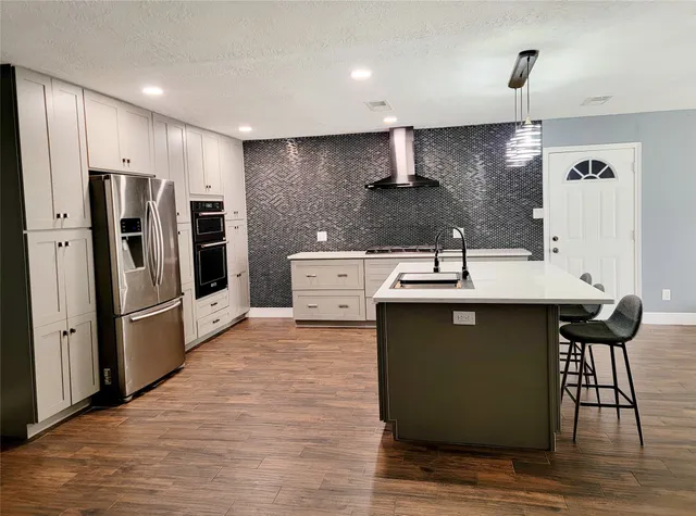 a kitchen with stainless steel appliances a sink a stove a refrigerator cabinets and a dining table with wooden floor