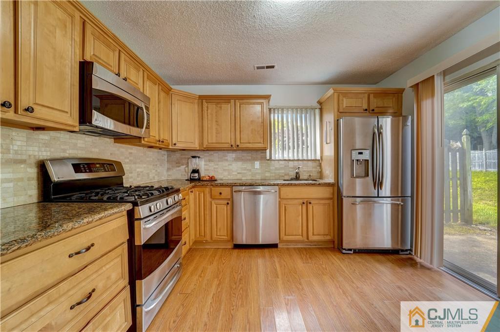 a kitchen with granite countertop wooden floors stainless steel appliances a stove a sink and a window