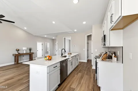 a kitchen with stainless steel appliances a stove a sink a refrigerator white cabinets and wooden floor