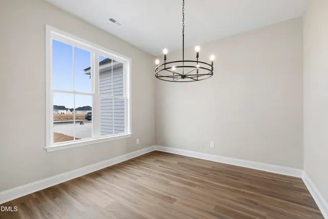 a view of empty room with wooden floor chandelier and window