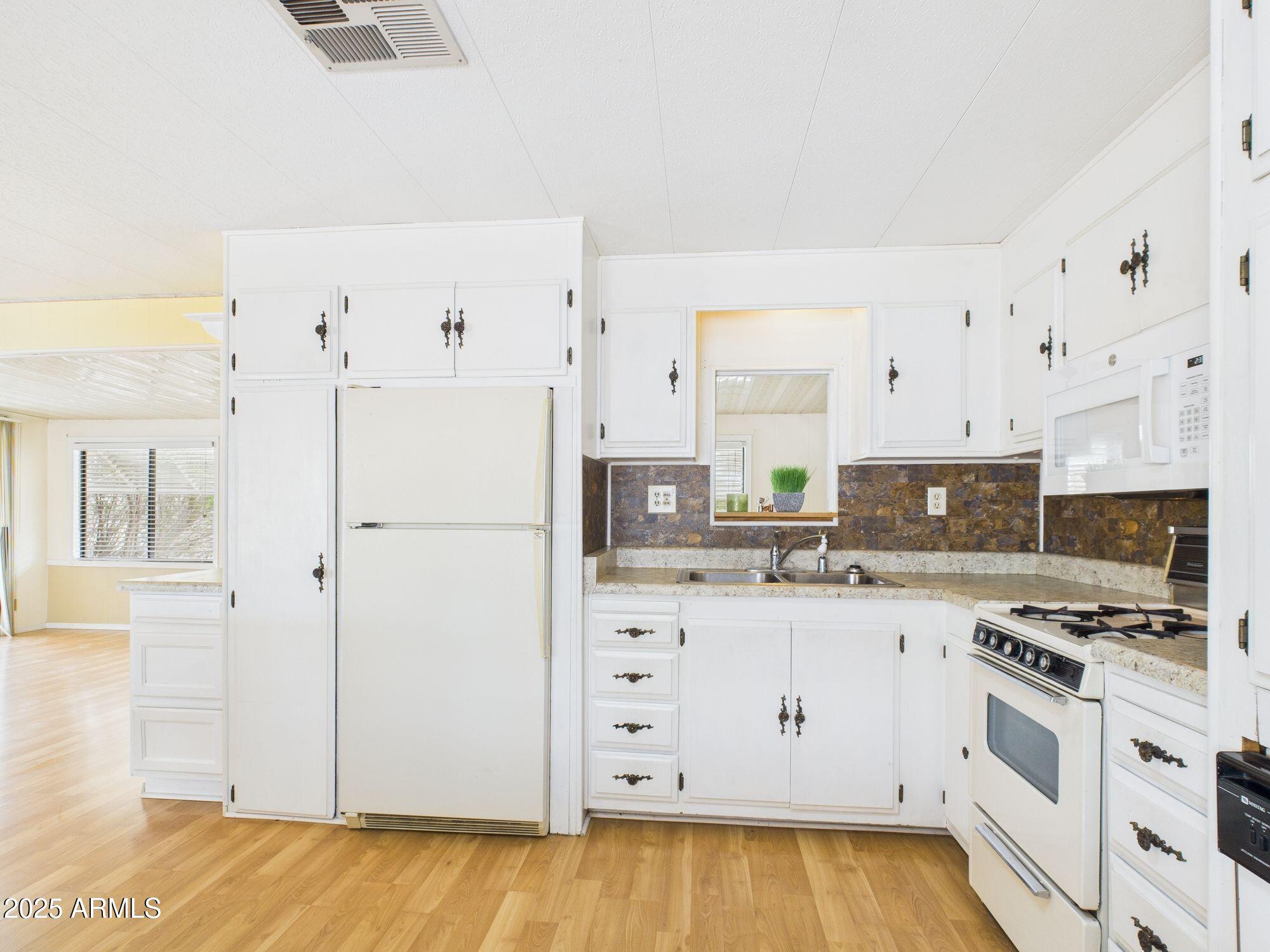 428 South 80th Way Mesa, AZ 85208 - Photo 10 of 21 a kitchen with granite countertop a refrigerator stove and white cabinets with wooden floor