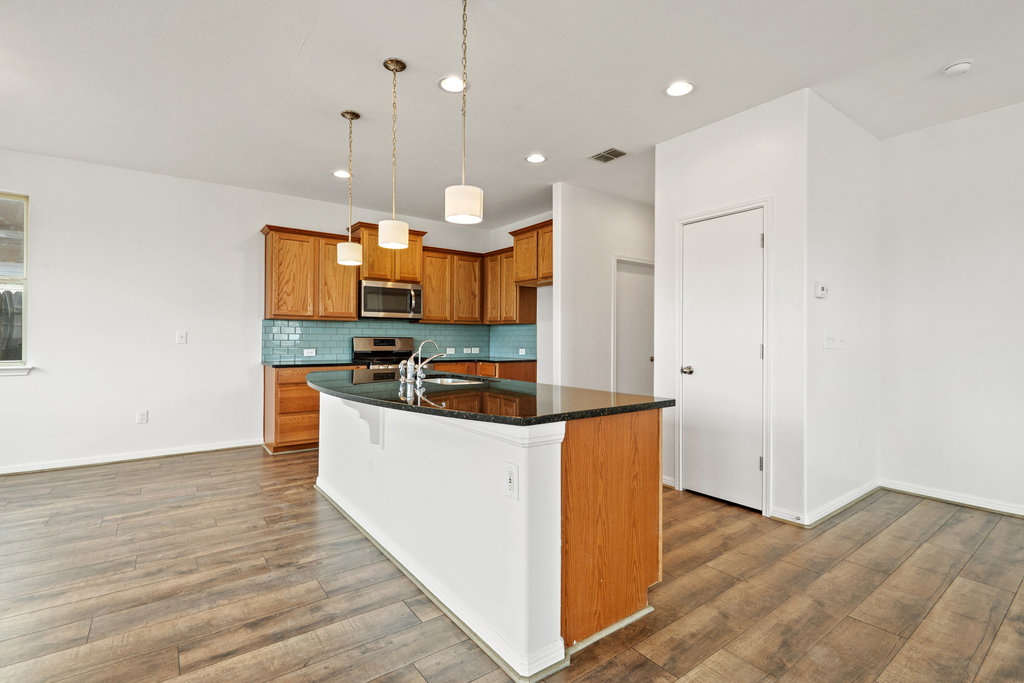 117 Wapiti Road Buda, TX 78610 - Photo 12 of 35 a kitchen with stainless steel appliances kitchen island granite countertop a stove a refrigerator a sink and a oven with wooden floor