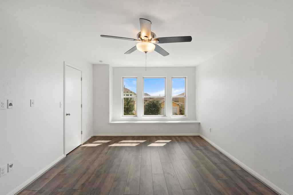 117 Wapiti Road Buda, TX 78610 - Photo 20 of 35 an empty room with wooden floor chandelier fan and windows