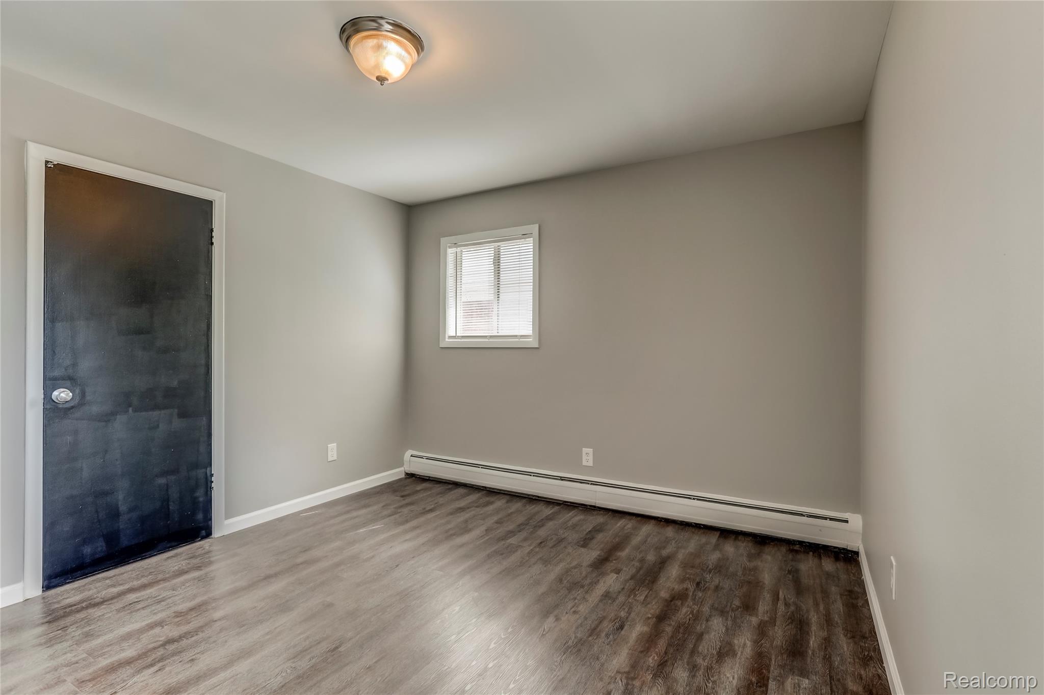 649 West Maple Road, Unit 8 Clawson, MI 48017 - Photo 6 of 16 Wood-finish flooring, neutral wall tones, semi-flush mount ceiling light, single window with blinds, and a dark-paneled door