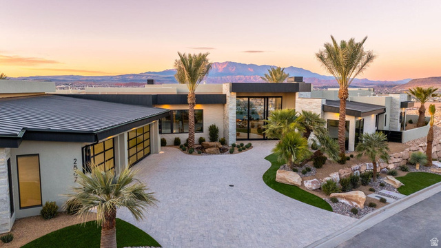 2867 East Granite Way St. George, UT 84790 - Photo 2 of 69 Contemporary desert-modern residence featuring a paver driveway, integrated landscaping with mature palm trees, a flat roofline, and expansive glass doors