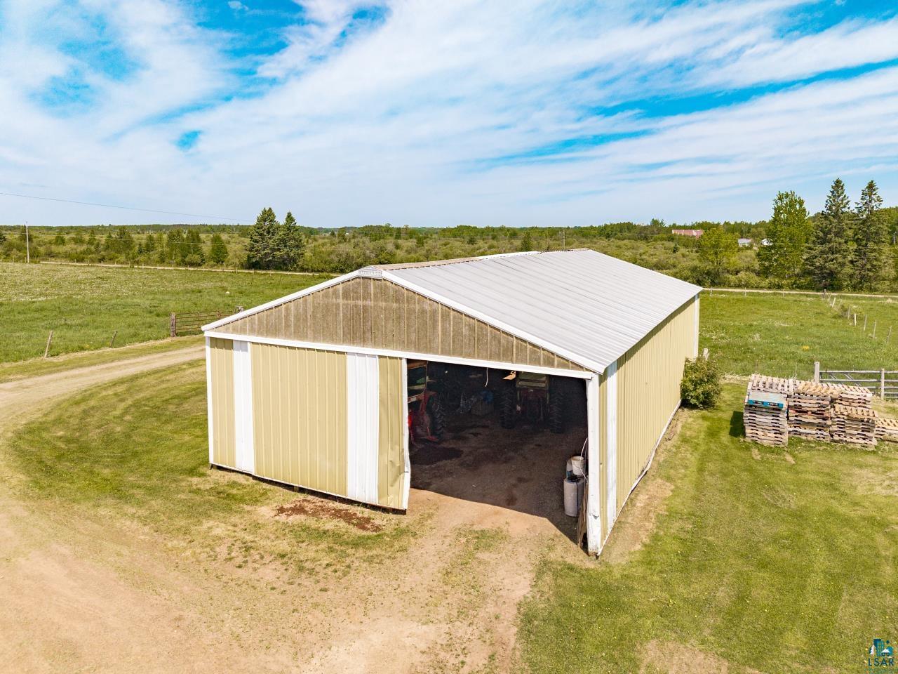 6606 Metso Road Kettle River, MN 55757 - Photo 34 of 84 Metal-sided pole barn with a light-colored roof, featuring a large open entrance and a natural dirt drive