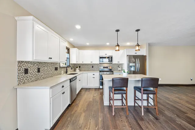 a kitchen with stainless steel appliances kitchen island granite countertop a wooden floor and white cabinets