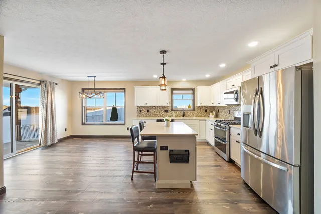 a kitchen with stainless steel appliances kitchen island granite countertop a refrigerator a stove oven and white cabinets with wooden floor