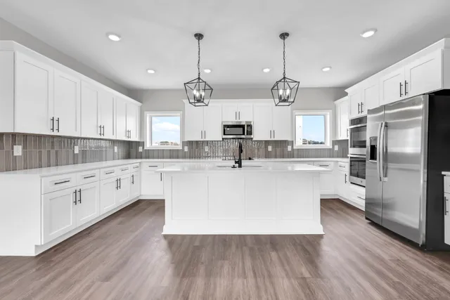 a large kitchen with granite countertop a large center island a sink dishwasher a refrigerator and white cabinets with wooden floor