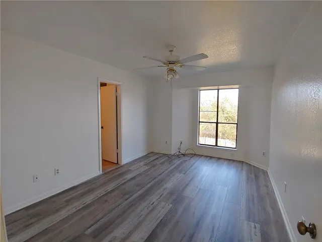 an empty room with wooden floor chandelier fan and windows