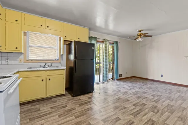 a kitchen with granite countertop a refrigerator a stove a sink and white cabinets with wooden floor