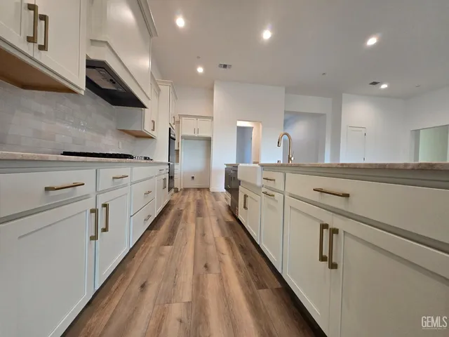 a kitchen with white cabinets a sink dishwasher and a stove with wooden floor