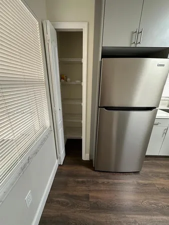 a view of a refrigerator in kitchen and an empty room with wooden floor